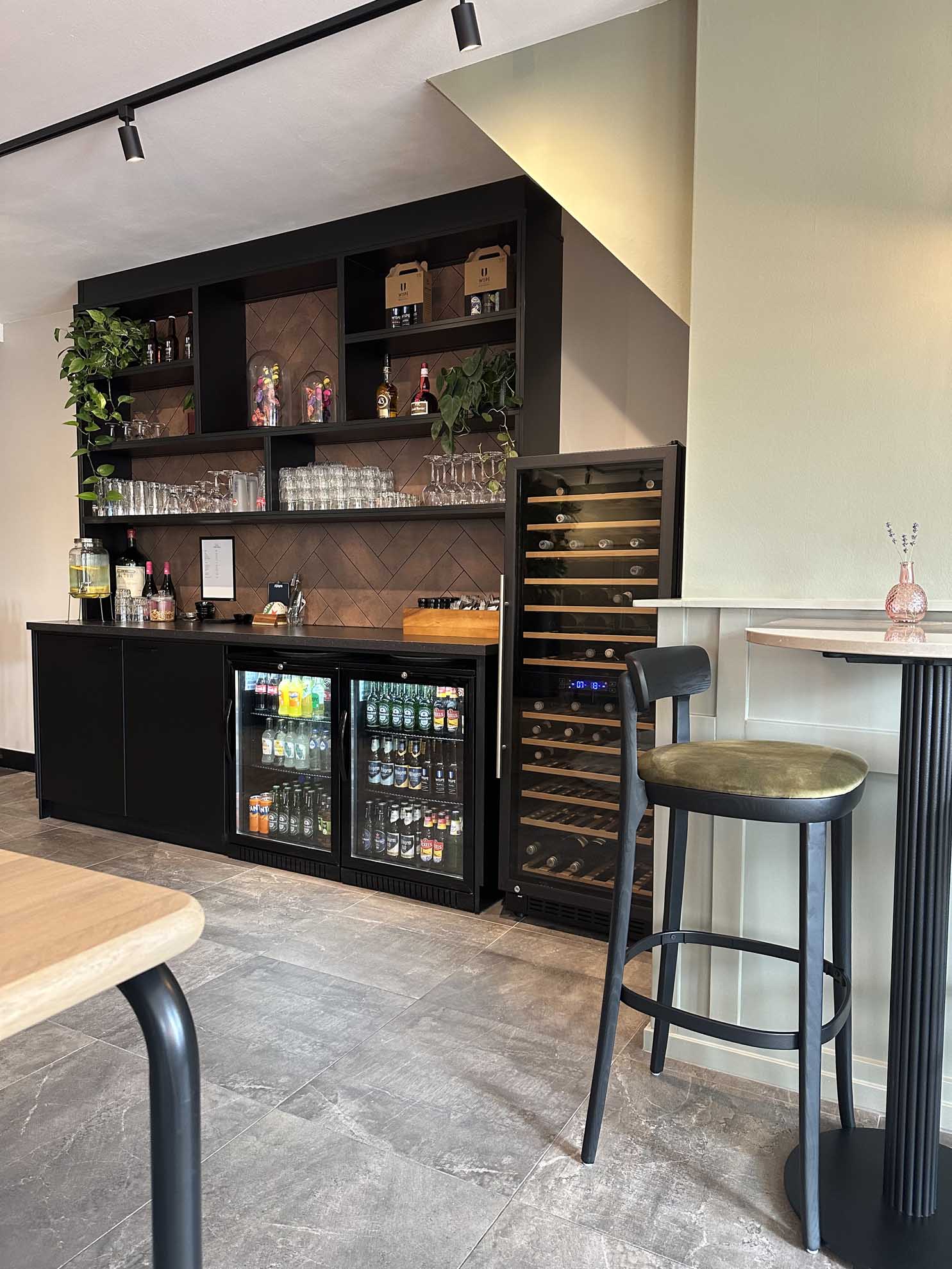 Bar met drankkoelkasten, wijnrek en glazen, met zitplaats in een moderne ruimte