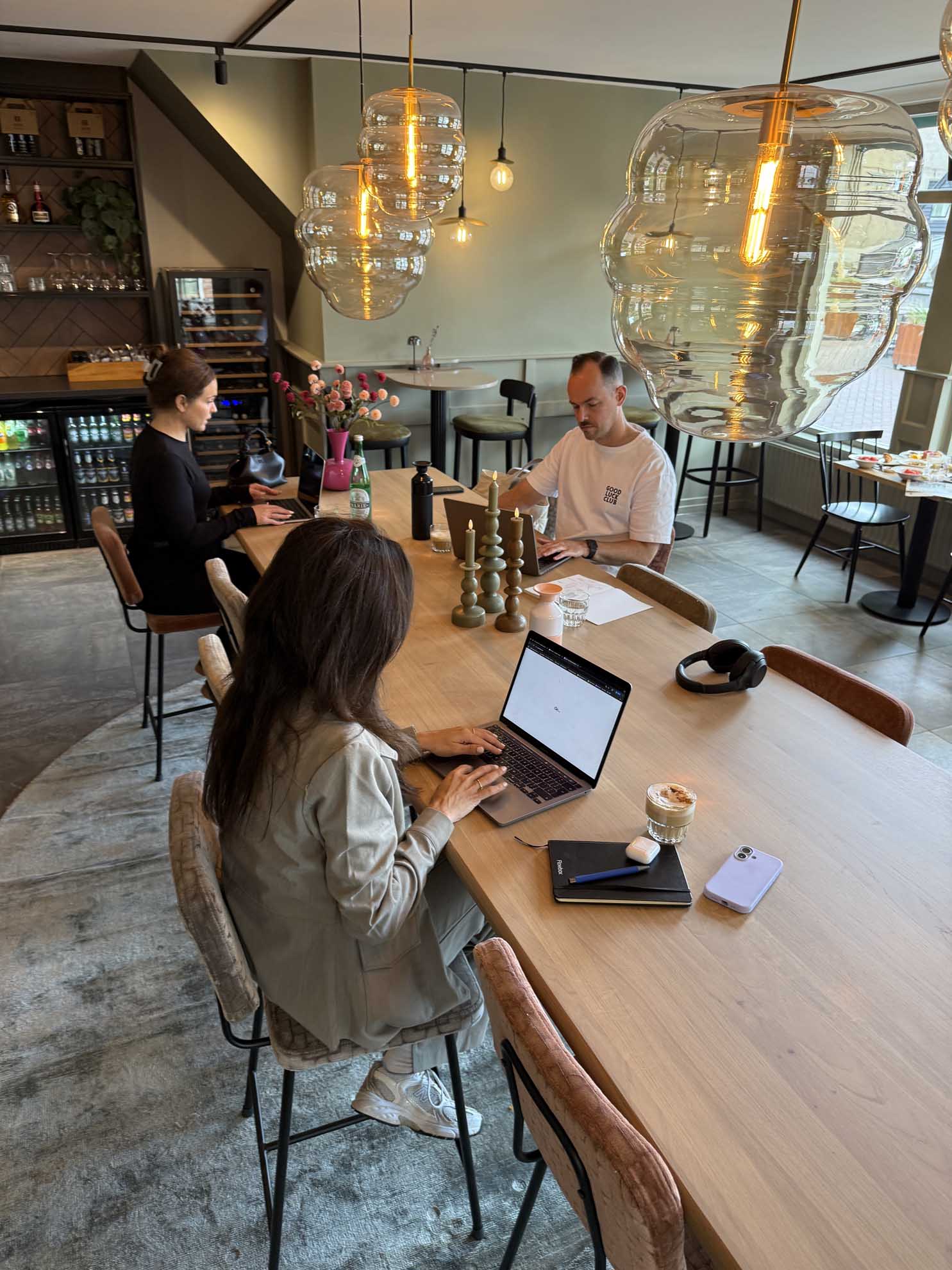Twee mensen werken aan een laptop en tablet in een moderne vergaderruimte met grote hanglampen