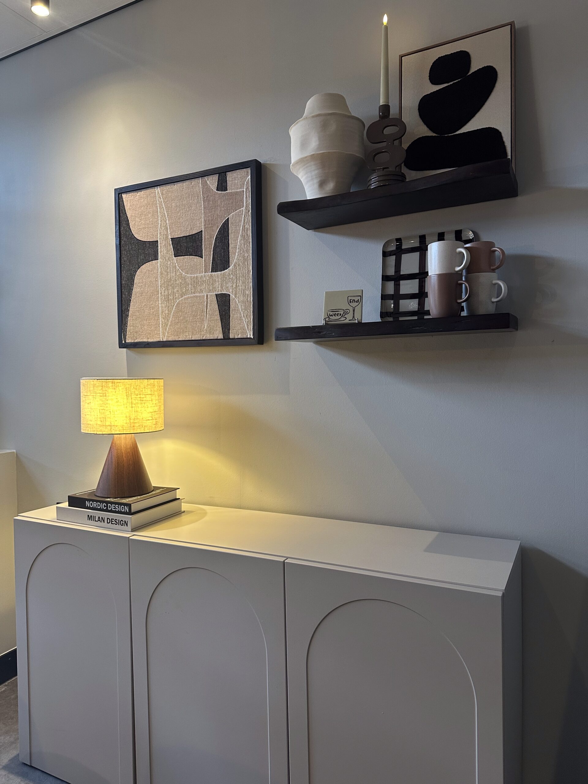 Interieurhoek met planken, abstracte wandkunst, een vaas, mokken en een lamp op een dressoir