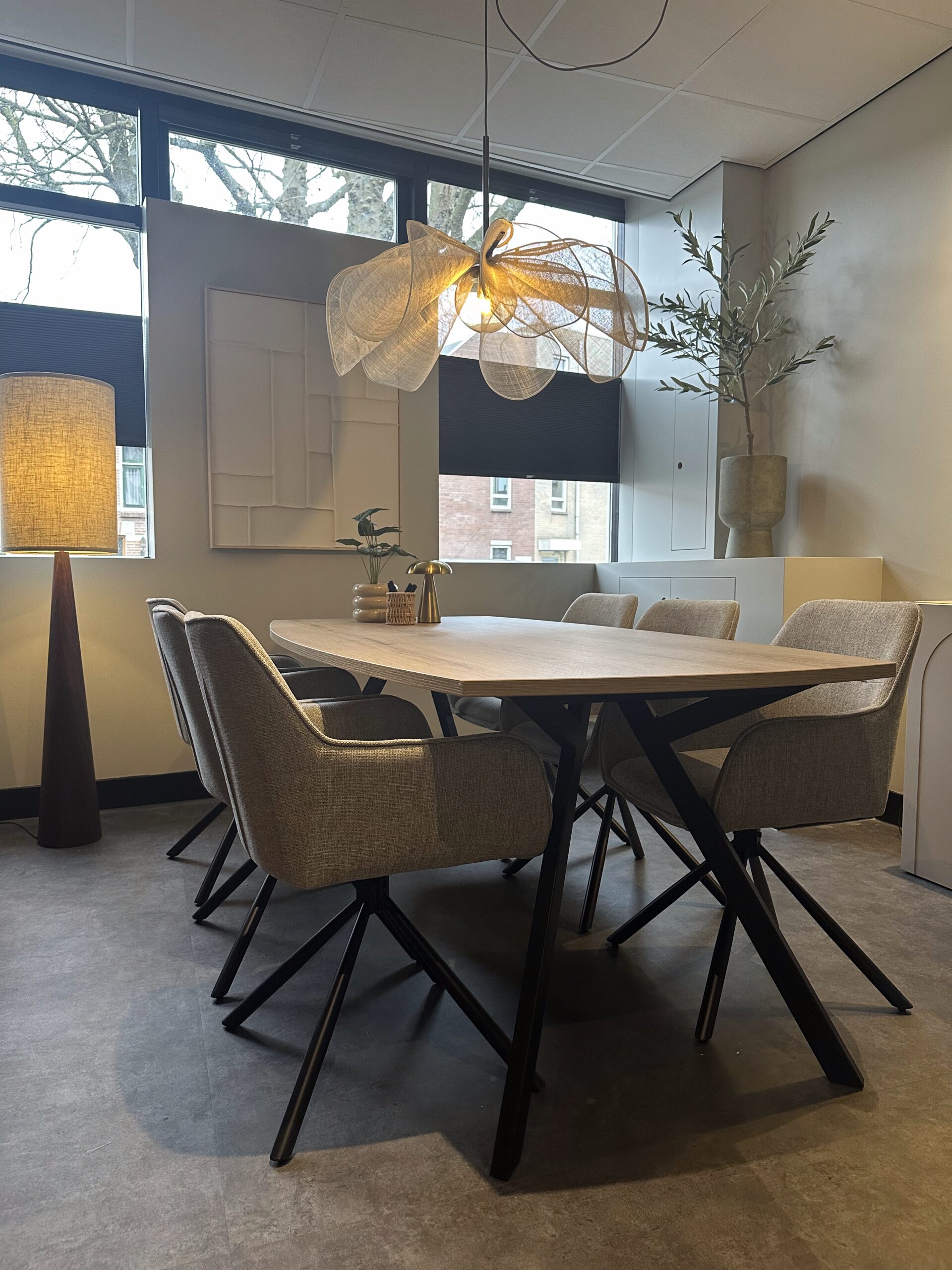 Ruime vergaderruimte met houten eettafel, gestoffeerde stoelen en een grote hanglamp boven de tafel